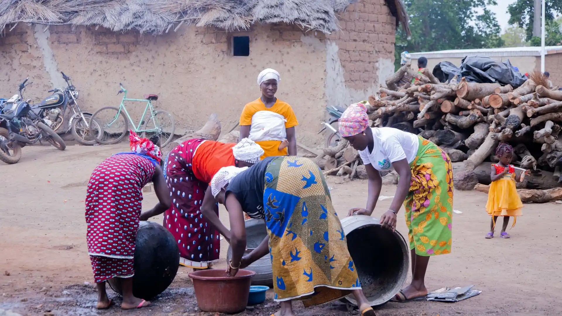 Dans la cour d'un village, quatre femmes en pagne lavent ensemble de grandes bassines