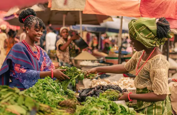 Deux femmes échangent des légumes-feuilles sur un marché en plein air