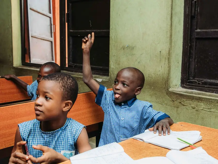 Deux écoliers en chemise à carreaux bleus assis en classe, cahiers ouverts ; l'un lève la main