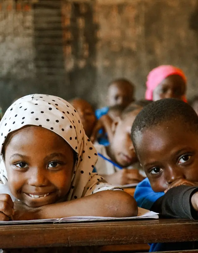 En classe, une écolière au foulard à pois sourit, son crayon à la main, à côté d'un camarade